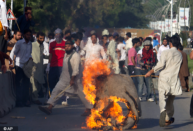 A Pakistani protester carries a burning piece of canvas towards containers police had placed to block the road leads to the diplomatic enclave in Islamabad, Pakistan on Thursday, Sept. 20, 2012. (AP Photo)