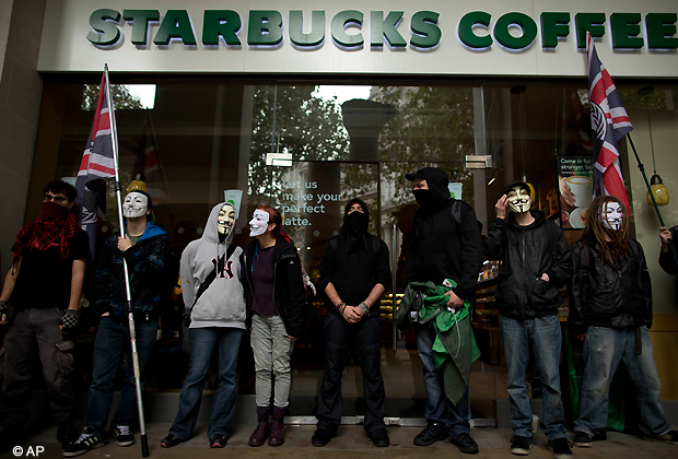 Demonstrators stand outside a branch of Starbucks as they gather near St Paul's Cathedral before the start of an anti austerity protest march through central London, Saturday, Oct. 20, 2012. (AP Photo)