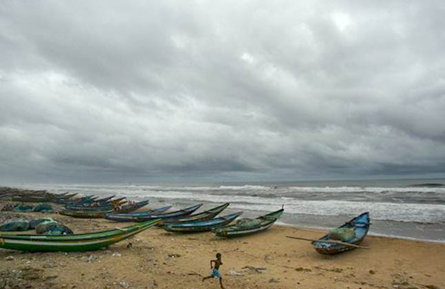 A young fisherman runs past fishing boats anchored on the shore after a cyclone alert, on the Bay of Bengal's Orissa coast in Puri, India, Wednesday, May 19, 2010. Cyclone Laila was expected to slam into the coast of southern India's Andhra Pradesh state from the Bay of Bengal on Thursday as the region braced for the worst storm in 14 years. (AP Photo/Biswaranjan Rout)