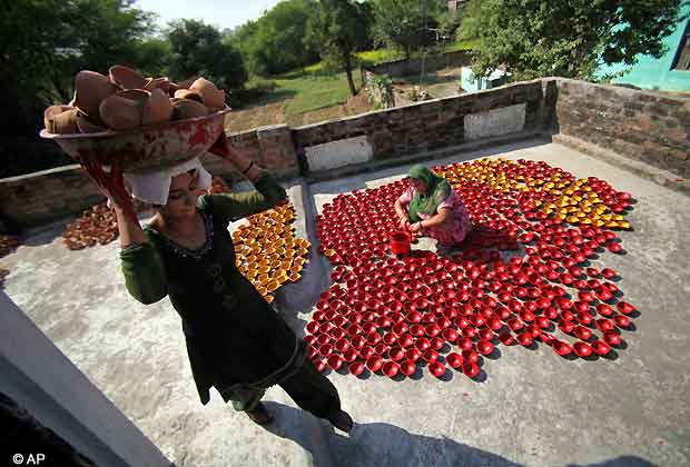 A potter carries earthen lamps on her head as another paints them ahead of the Hindu festival Diwali on the outskirts of Jammu, Nov. 6, 2012. Diwali, the festival of lights, will be celebrated on Nov.13. (AP Photo)