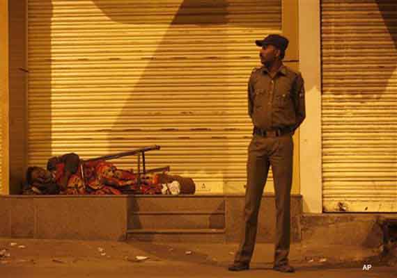 An Indian homeless man rests in front of closed shops , as a policeman stands guard in Hyderabad, India, Friday, Nov. 16, 2012. At least seven people were injured after violence broke out near the landmark Charminar Friday over a temple row, according to news reports. (AP Photo/Mahesh Kumar A.)