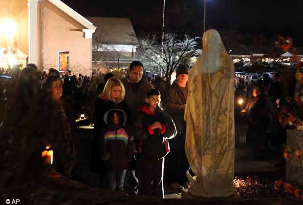 A family prays at a statue of the Virgin Mary outside Saint Rose of Lima church, Friday, Dec. 14, 2012 in Newtown, Conn. A man killed his mother at home and then opened fire Friday inside the elementary school where she taught, massacring 26 people, including 20 children, as youngsters cowered in fear to the sound of gunshots echoing through the building and screams coming over the intercom.