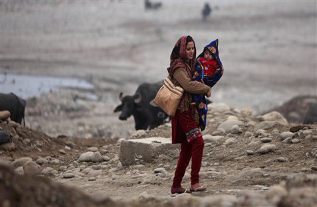 An Indian woman carries her son, wrapped in warm clothes, and walks on the banks of the River Tawi on a cold and foggy morning in Jammu, India, Sunday, Jan. 6, 2013. More than 100 people have died of exposure as northern India deals with historically cold temperatures. (AP Photo/Channi Anand)