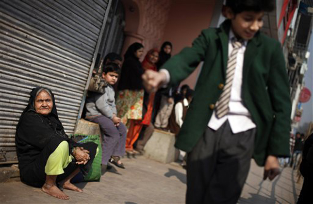 An elderly Indian Muslim woman sits against a closed shop while a school boy imitates a marching soldier as they wait for the annual Republic Day parade rehearsal to move past them in New Delhi, India, Wednesday, Jan. 23, 2013. India celebrates Republic Day annually on Jan. 26. (AP Photo/Altaf Qadri)