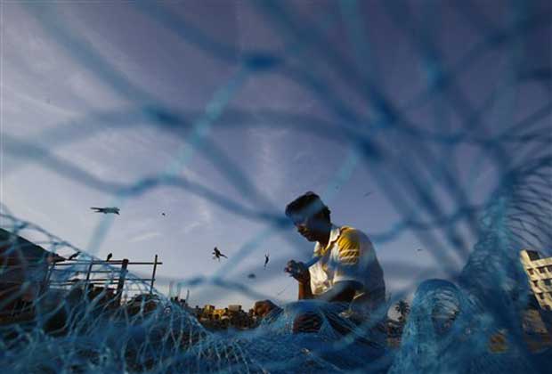 An Indian fisherman repairs a fishing net on the Arabian Sea coast in Mumbai, India, Tuesday, March 19, 2013.(AP Photo)