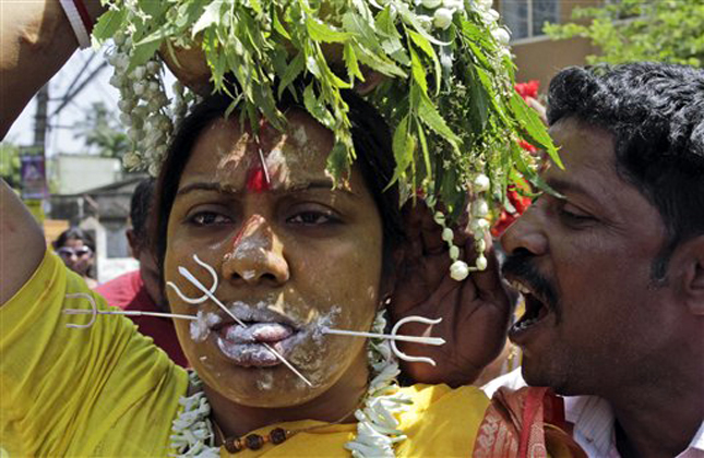 A Hindu devotee shouts into the ear of a woman devotee, tongue and cheek pierced with metal rods, as she participates in a religious procession during a chariot festival dedicated to Goddess Mutthumariamman in Bandel, about 55 kilometers (34 miles) from Kolkata, India, Friday, April 5, 2013. The ritualistic acts of inflicting pain on oneself are performed as an act of penance with the belief that it will prevent diseases and for the well being of the families of devotees. (AP Photo/Bikas Das)