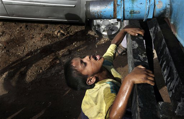 An Indian boy drinks water dripping from a government tanker supplying water to residents of a colony in New Delhi, India, Thursday, May 23, 2013. Many areas of the Indian capital are facing acute water shortage, a repeated annual phenomenon during summer when taps go dry as demand rises. (AP Photo/Manish Swarup)
