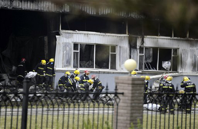 Firemen carry out bags containing bodies of those killed at a poultry processing plant that was engulfed by a fire in northeast China's Jilin province's Mishazi township on Monday, June 3, 2013. The massive fire broke out here early Monday, trapping workers inside a cluttered slaughterhouse and killing over a hundred people, reports and officials said. (AP Photo) CHINA OUT