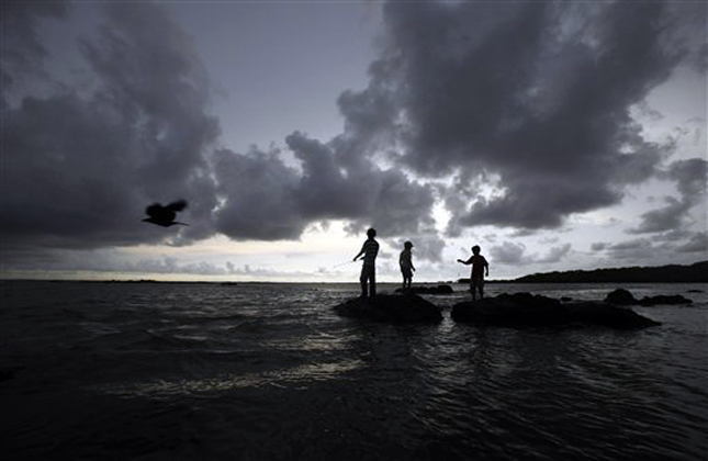 Boys try to catch fish along the shores of the Arabian Sea as rain clouds hover over in Mumbai, India, Monday, June 3, 2013. The monsoon rains, crucial for India's agriculture arrived in the southern Kerala state Saturday and is expected to advance northwards. (AP Photo/Rafiq Maqbool)