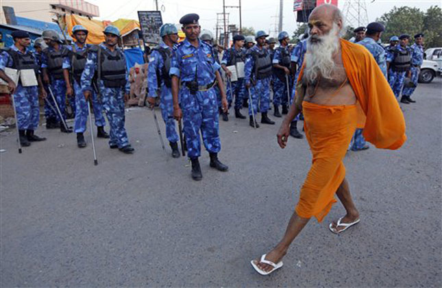 Holy man walks past security personnel standing guard in Ayodhya, India, Saturday, Aug. 24, 2013. Security has been tightened in the area to enforce a ban on the procession call by the Hindu right winged Vishwa Hindu Parishad, or World Hindu Council, which aims at expediting the movement for construction of the Ram Temple in Ayodhya. (AP Photo)