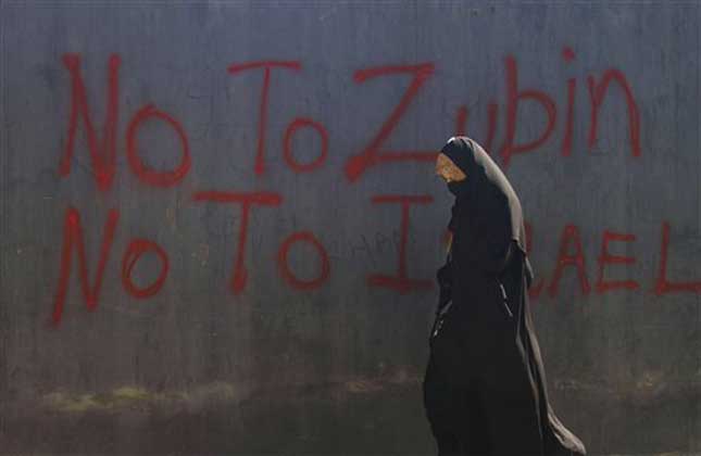A Kashmiri woman walks past graffiti against a concert by renowned orchestra conductor Zubin Mehta in Srinagar on Friday, Sept. 6 (AP Photo)