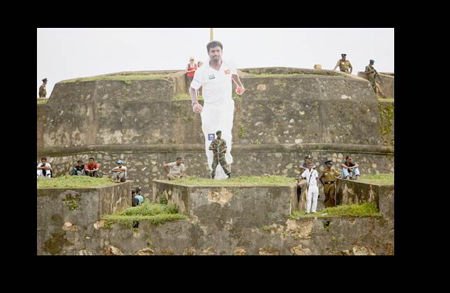 Security personnel and spectators look on next to a giant cutout of Sri Lankan spin bowler Muttiah Muralitharan erected on a 17th century Dutch built fortress during the third day of the first test cricket match between India and Sri Lanka in Galle, Sri Lanka, Tuesday, July 20, 2010. (AP Photo/Eranga Jayawardena)