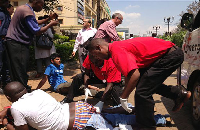 An injured man is trreated outside an upscale shopping mall, seen background, in Nairobi, Kenya, where shooting erupted when armed men attempted to rob a shop, according to police. (AP Photo)