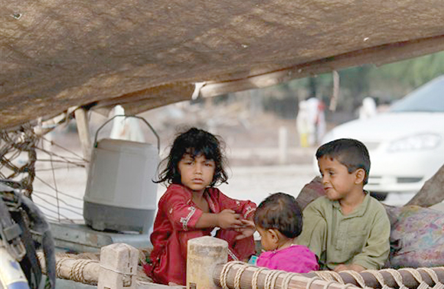 Little flood survivors sit in a makeshift tent set up on the mid section of a main highway in Kamp Koroona village near Nowshera, Pakistan on Monday, Aug. 2, 2010. The government has deployed thousands of soldiers and civilian rescue workers to save people trapped by the floodwaters, distribute food and collect the bodies of the dead. (AP Photo/Anjum Naveed)