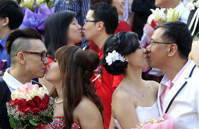 Newly wed couples kiss each other as they pose for photographers during a mass wedding ceremony on Valentine's Day and Chap Goh Mei festival. (AP Photo)