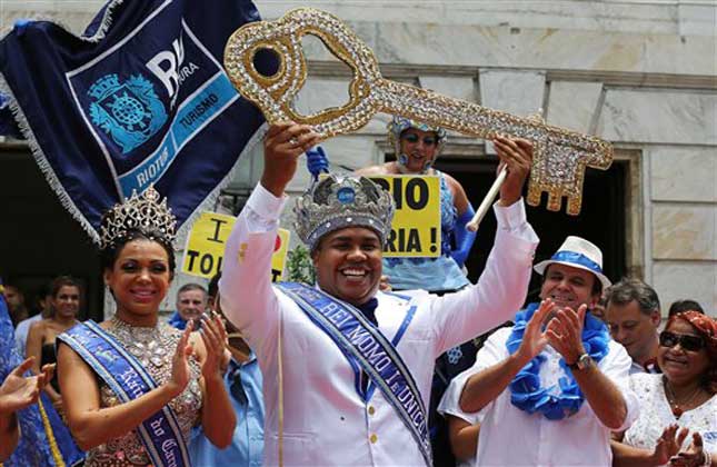 Flanked by Carnival Queen Leticia Martins Guimaraes and Rio de Janeiro's Mayor Eduardo Paes, a crowned and costumed Wilson Dias da Costa Neto, the 2014 King Momo or Carnival King, holds up the key to the city at a ceremony marking the official start of Carnival, in Rio de Janeiro, Brazil. (AP Photo)