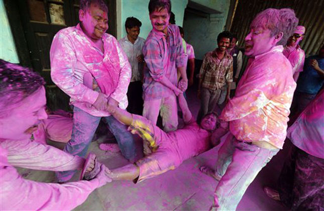 People with their faces smeared with color and glitter, lift a man during Holi celebrations at Loknath, in Allahabad. (AP Photo)