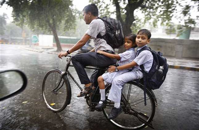 A man rides a bicycle with two children returning from school as it rains in New Delhi, India, Wednesday, July 2, 2014.