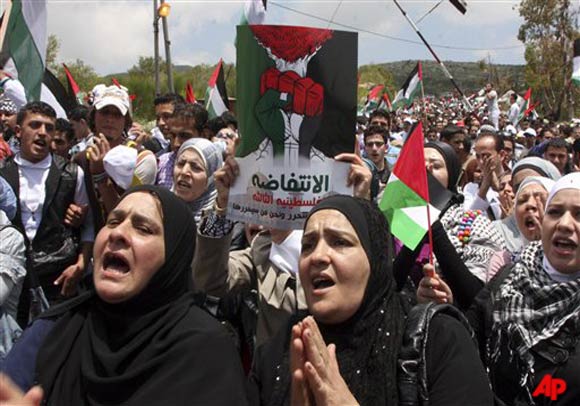 Palestinian protesters carry Palestinian flags as they shout slogans marking the 63rd anniversary of the mass displacement of Palestinians surrounding Israel's establishment in 1948, in the town of Ein al Tineh accross from the Golan Heights, Syria, Sunday, May 15, 2011. The Israeli military said thousands of protesters approached Syria's border with the Israeli controlled Golan Heights. It said hundreds of people burst through the border, and soldiers opened fire to stop them. Dozens were wounded and six were reported killed. The Arabic on banner reads the third Palestinian uprising. (AP Photo/Bassem Tellawi)