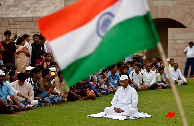 The flag of Indian is seen in the foreground as rights activist Anna Hazare sits in a meditative posture at Rajghat, the Mahatma Gandhi memorial in New Delhi, India, Monday, Aug. 15, 2011. Hazare announced he will resume his hunger strike on Tuesday to pressure the government into enacting stronger legislation for an anti corruption watchdog. On Monday, police in Delhi denied Hazare permission for his hunger strike, but supporters said they will fast anyway and risk arrest. (AP Photo/Gurinder Osan)