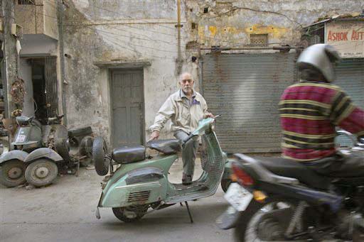 In this Feb. 18, 2010 photo, Prem Kalra, 72, looks on with his old Bajaj super scooter, as a motorcyclist moves past in New Delhi, India. Once there was the waiting list to buy Bajaj scooters, a wait which often lasted for years. There was the pride of that first ride and you knew that you'd finally made it to the middle class. Later this month, Bajaj's last scooter will roll out from its factory, ending an era in India's transition from dreary socialist economy into a consumerist power house.(AP Photo/Manish Swarup)