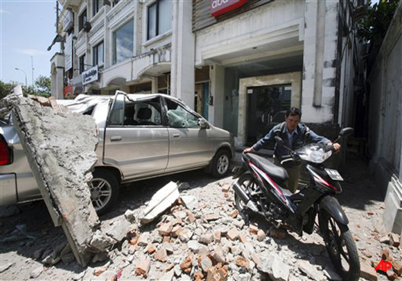 A man pushes his motorbike away in the fallen debris of a building damaged by an earthquake in Kuta, Bali, Indonesia, Thursday, Oct. 13, 2011. The 6.1 magnitude earthquake jolted Indonesia's popular resort island of Bali on Thursday, causing widespread panic and injuring at least 50 people, many with broken bones and head wounds. (AP Photo/Firdia Lisnawati)