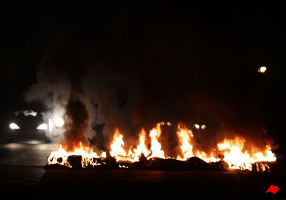 Motorists approach a barricade of burning tires late Saturday, Dec. 17, 2011, in the western village of Karzakan, Bahrain. Protests and clashes between anti government youths and riot police were reported Saturday in numerous Shiite Muslim villages in Bahrain. (AP Photo/Hasan Jamali)