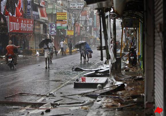 People walk past fallen sign boards and other trash caused by heavy winds in Pondicherry, India, Friday, Dec. 30, 2011. India's weather office has warned residents along parts of the country's southeastern coast that Cyclone Thane is likely to cause heavy rains and gale force winds. (AP Photo/Aijaz Rahi)