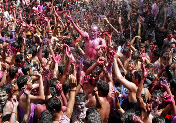 Indians, their faces smeared with color and glitter, dance as water is sprinkled on them during Holi celebrations in Allahabad, India, Thursday, March 8, 2012. Holi, the Hindu festival of colors, also heralds the coming of spring. (AP Photo/Rajesh Kumar Singh)