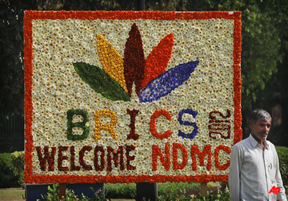 An Indian worker walks past a sign made of fresh flowers with the BRICS Summit logo on it in New Delhi, India, Wednesday, March 28, 2012. The BRICS Summit which includes the nations of Brazil, India, Russia, China and South Africa is on March 29th. (AP Photo/Kevin Frayer)