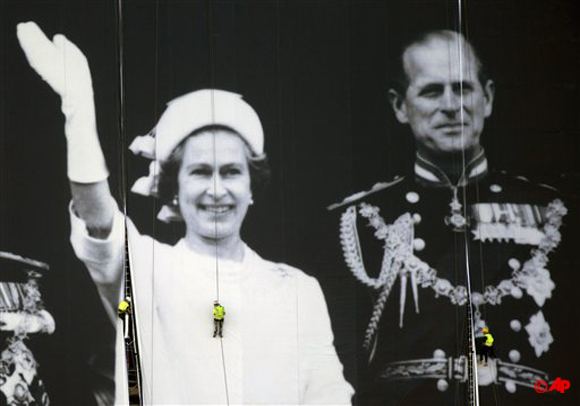 Workers help to hang a giant image from a building on the south bank of the River Thames showing Britain's Queen Elizabeth II, left, and her husband Prince Phillip, standing on the balcony of Buckingham Palace during the Queen's 1977 Silver Jubilee, Friday, May 25, 2012. The giant canvas, measuring 100 meters by 70 meters and weighing nearly two tons, was officially unveiled on Friday and will be displayed until the end of June, in celebration of the Diamond Jubilee, marking the Queen's 60 year reign. (AP Photo/Matt Dunham)