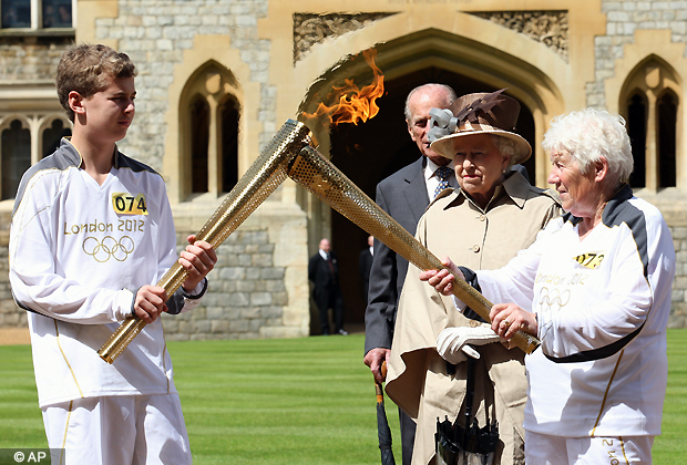 This image made available by LOCOG shows Queen Elizabeth II, second right, and the Duke of Edinburgh watching the Torch Kiss as Torchbearer 073 Gina Macgregor, right, passes the Olympic Flame to Torchbearer 074 Phillip Wells, left, outside Windsor Castle, Windsor, England Tuesday July 10, 2012. (AP Photo/Chris Radburn/LOCOG)