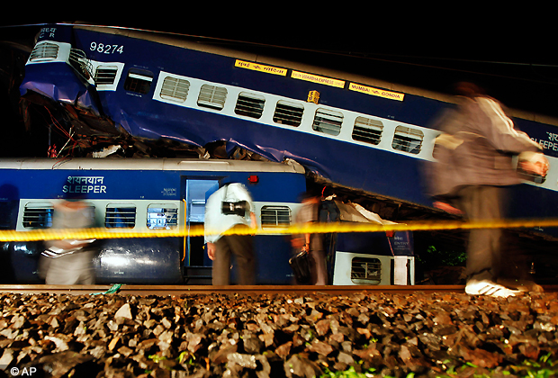 People walk next to wrecked rail cars in Kasara, India, Friday, July 20, 2012. Vidarbha express collided with some derailed coaches of a commuter train that were lying on the tracks Thursday. (AP Photo/Rajanish Kakade)