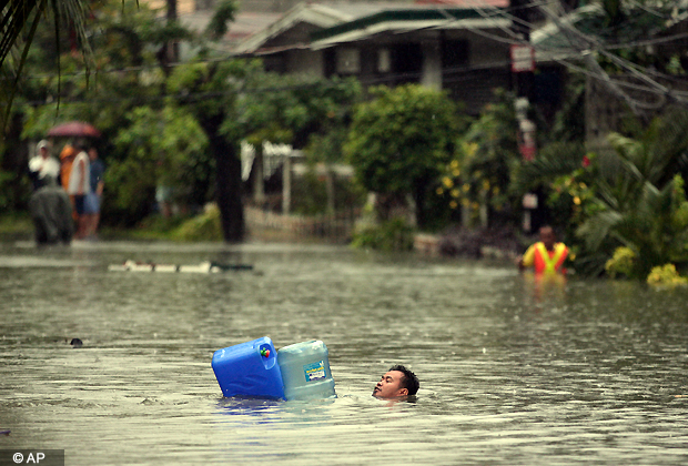 A man crosses deep floodwaters using water containers as floaters in suburban Quezon City, north of Manila, Philippines on Tuesday Aug. 7, 2012. Torrential rains pounding the Philippine capital on Tuesday paralyzed traffic as waist deep floods triggered evacuations of tens of thousands of residents and the government suspended work in offices and schools.(AP Photo)