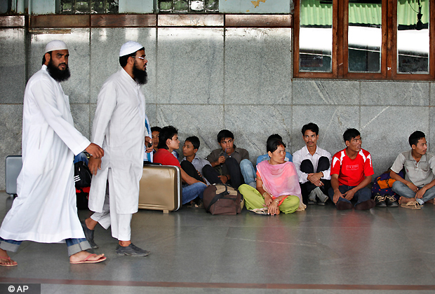 Muslims walk past people from India's northeastern states waiting to board trains to go back home, at a train station in Bangalore, India, Thursday, Aug. 16, 2012. Thousands of Indians from the northeast are fleeing the southern city of Bangalore, spurred by rumors they would be attacked in retaliation for communal violence in their home state of Assam. (AP Photo)