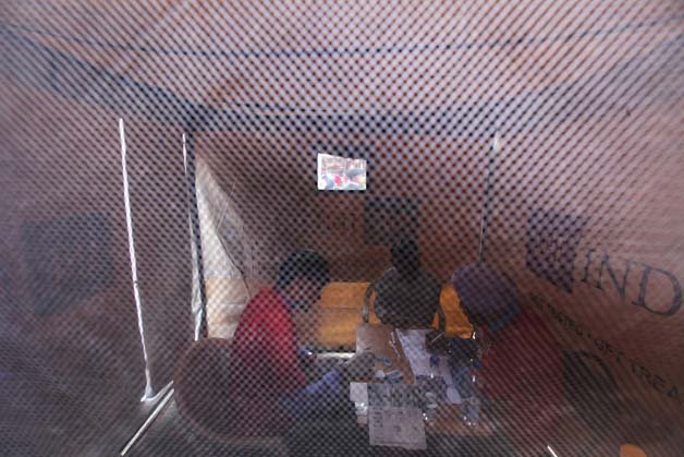 Indian counselors from AIDS Healthcare Foundation, or AHF, examine the blood of a person to determine if it is infected by HIV or not, as seen through a mesh window, during an awareness program on International Condom Day in New Delhi.